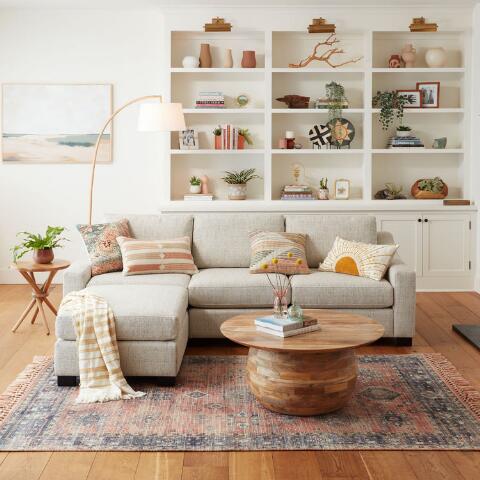 wood round coffee table with pedestal base in a living room with sectional sofa. 