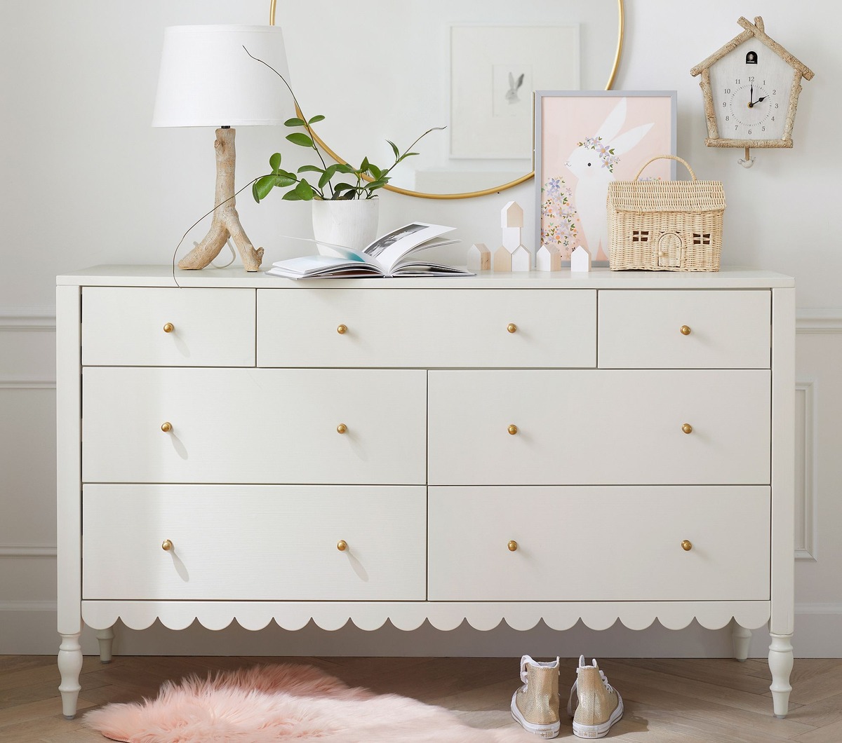 white scalloped dresser with gold knobs and decorative items on top. 