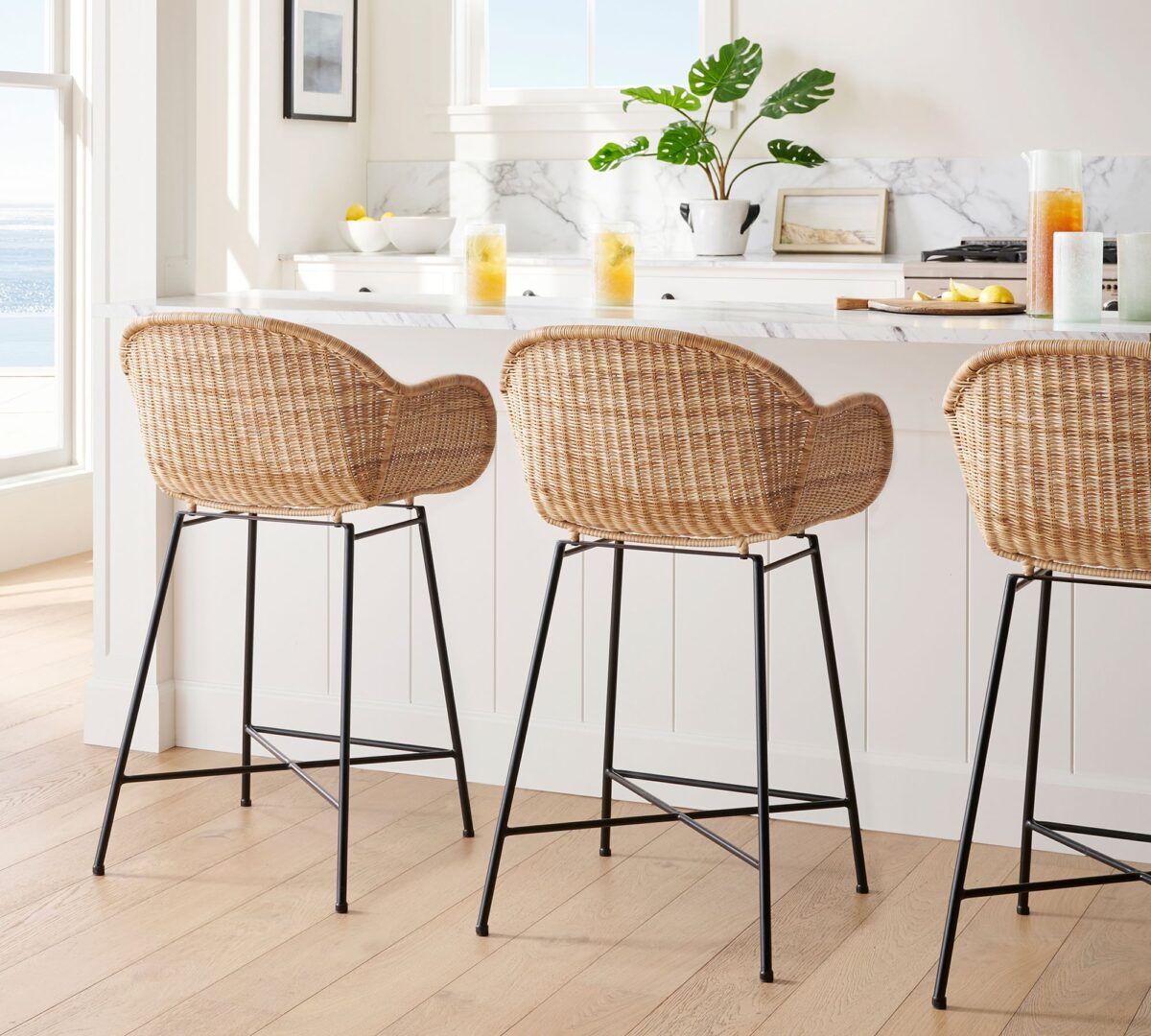 3 rattan bar stools with black metal legs at a kitchen island. 