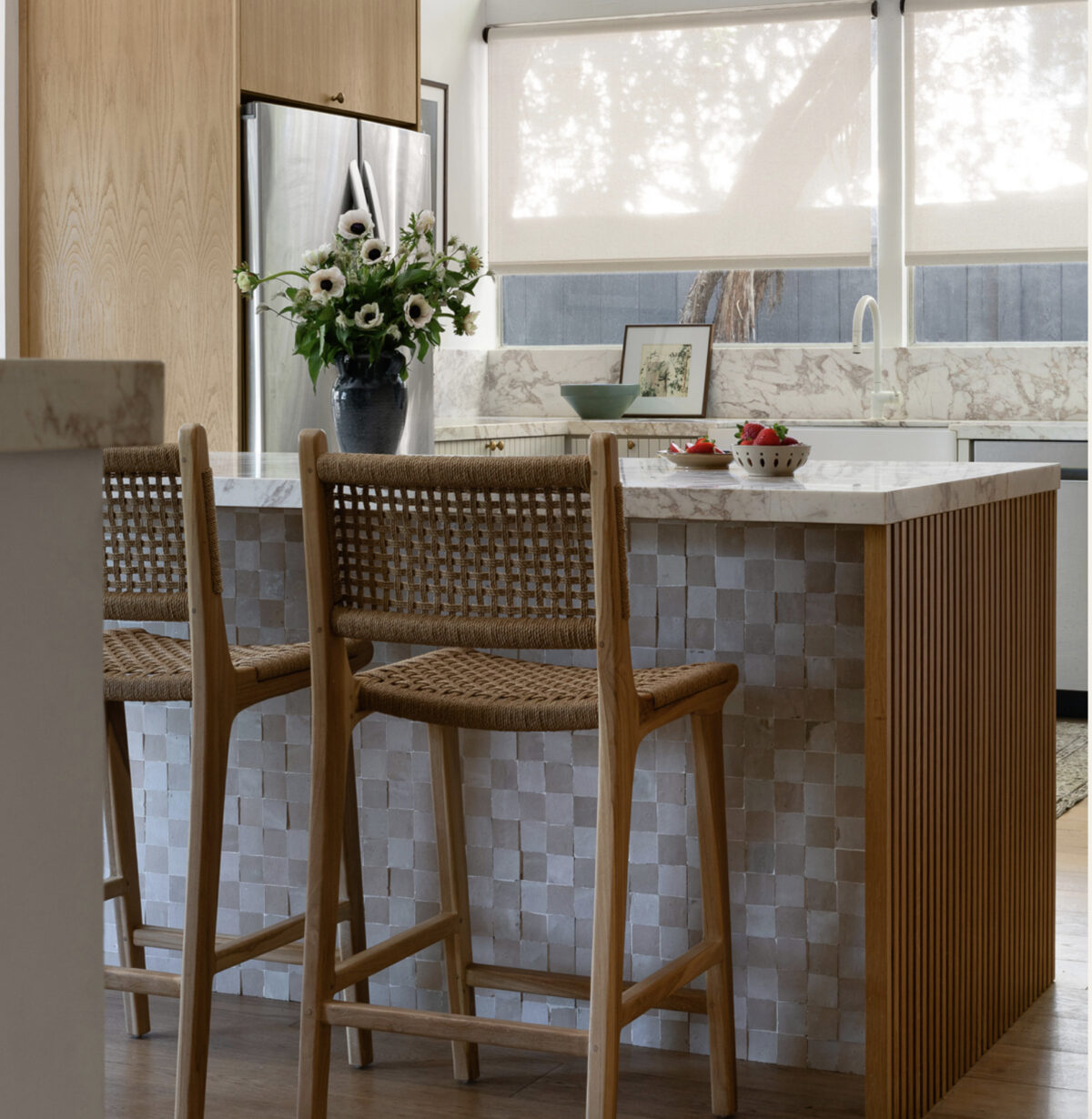 a rattan counter height stool at a checkered kitchen island with fruit and flowers. 