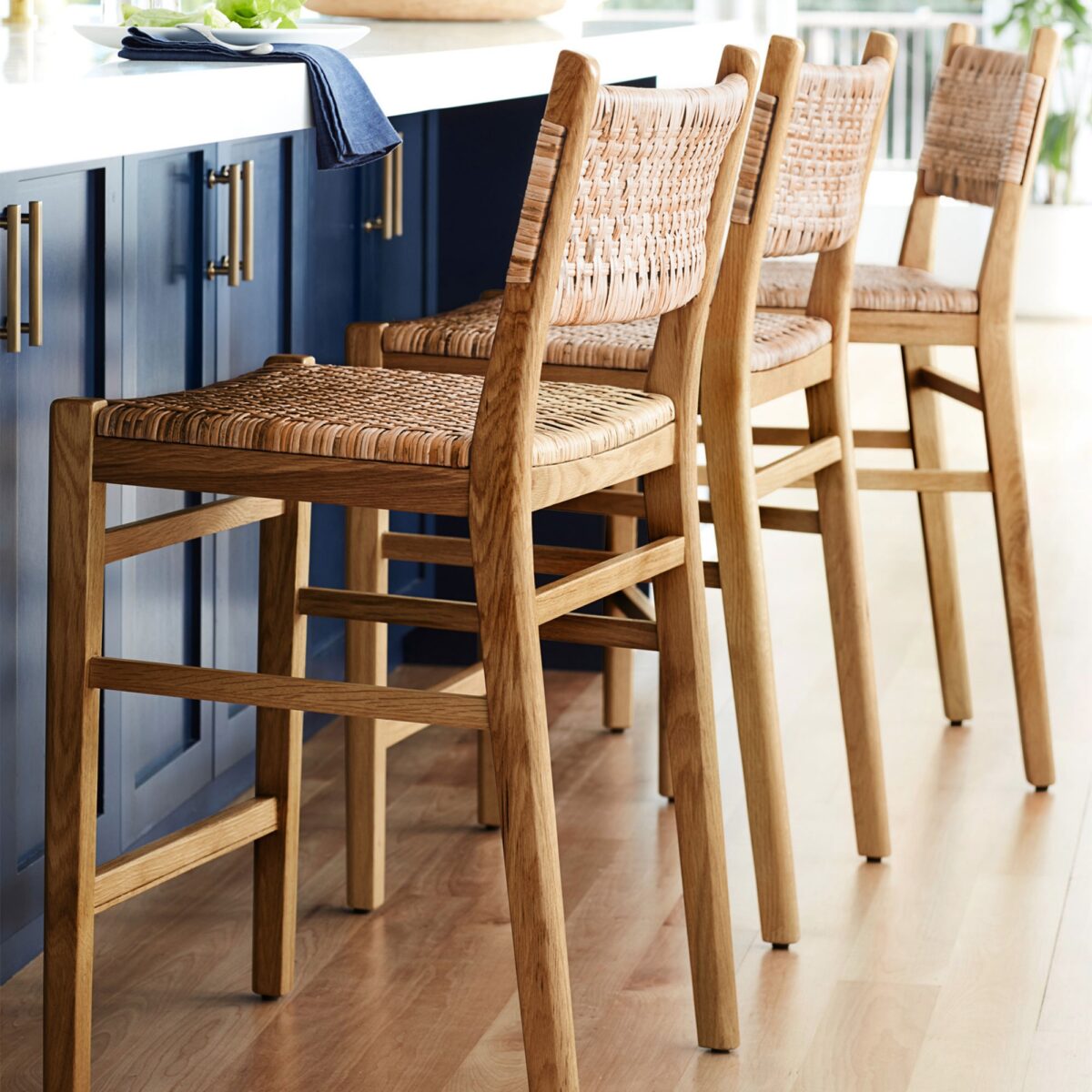 3 woven rattan bar stools at a kitchen island in a blue kitchen. 